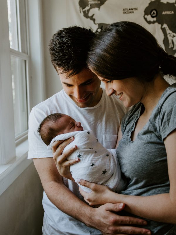 Young Florida couple smiling while holding their newborn in their new home—helped by Elite Lending mortgage experts