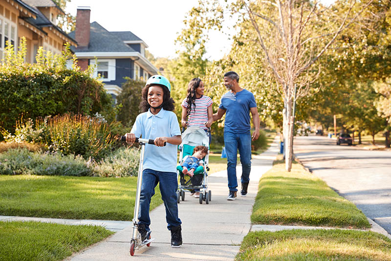 Couple,Push,Daughter,In,Stroller,As,Son,Rides,Scooter